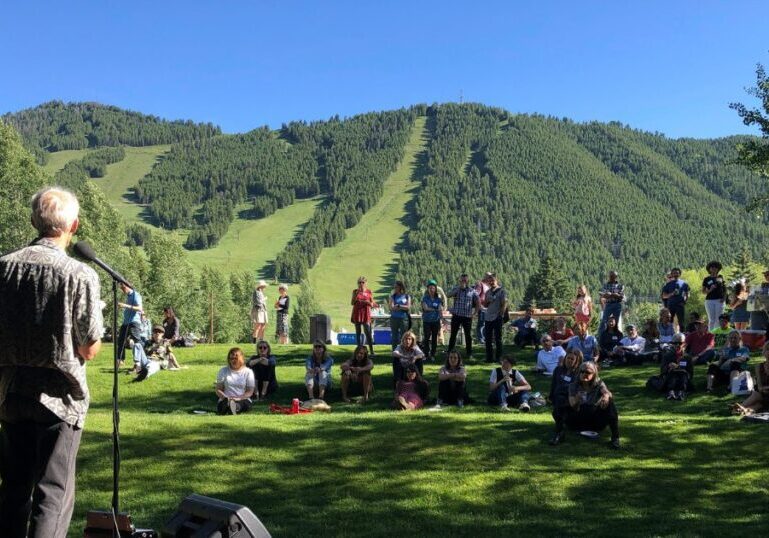 Writers gathered outdoors for a reading in Jackson Hole, with forested mountains behind